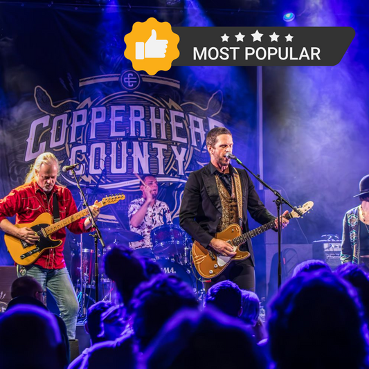 A band performing on stage in front of a custom backdrop with a design featuring the band and the text 'Copperhead County'. The backdrop is predominantly black with a graphic design in vibrant colors.