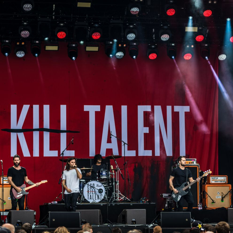A band performing on stage in front of a large red backdrop with the text 'KILL TALENT' printed in white.