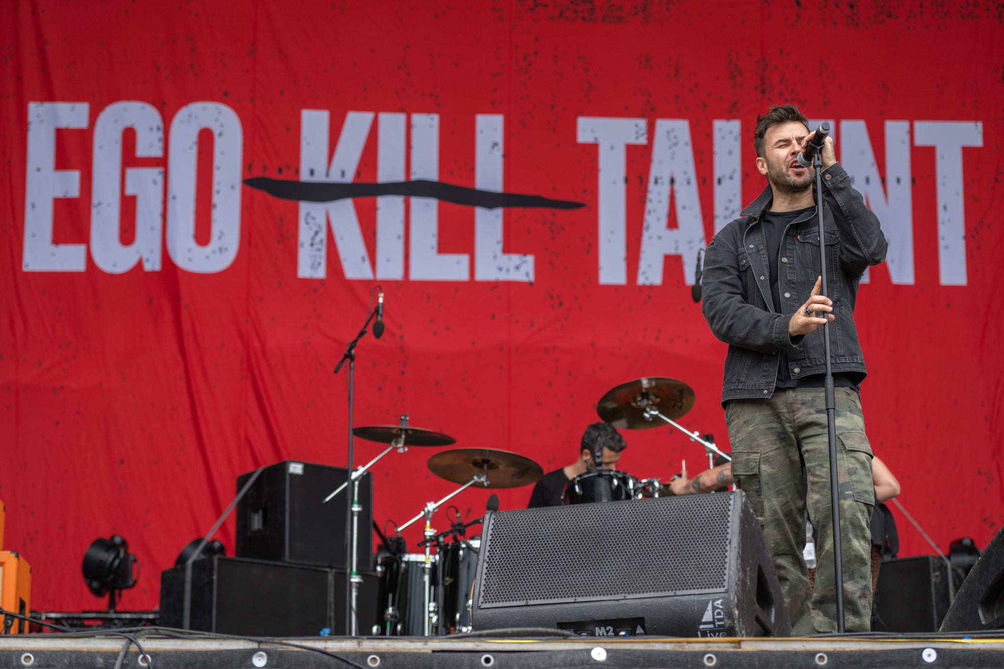 A band performing on stage with a red backdrop featuring the text 'EGO KILL TALENT'.