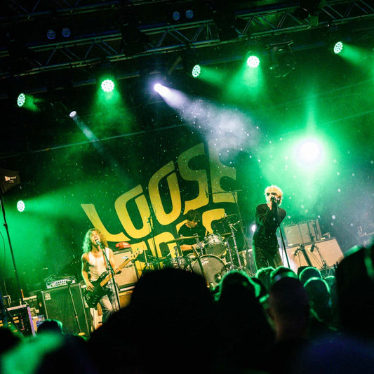 A band performing in front of a custom fabric backdrop with the words Loose Ends on it