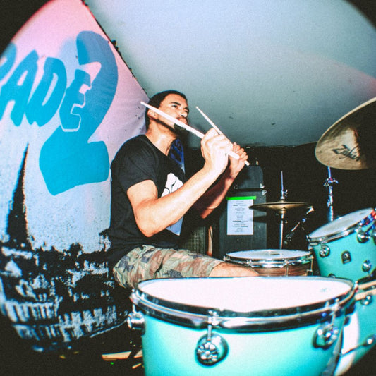 A drummer performing in front of a custom backdrop designed for a band, with eyelets visible for hanging.