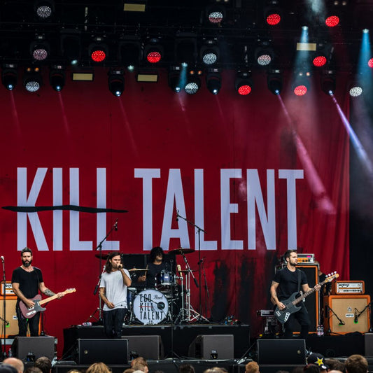 A band performing on stage in front of a large red backdrop with the text 'KILL TALENT' printed in white.